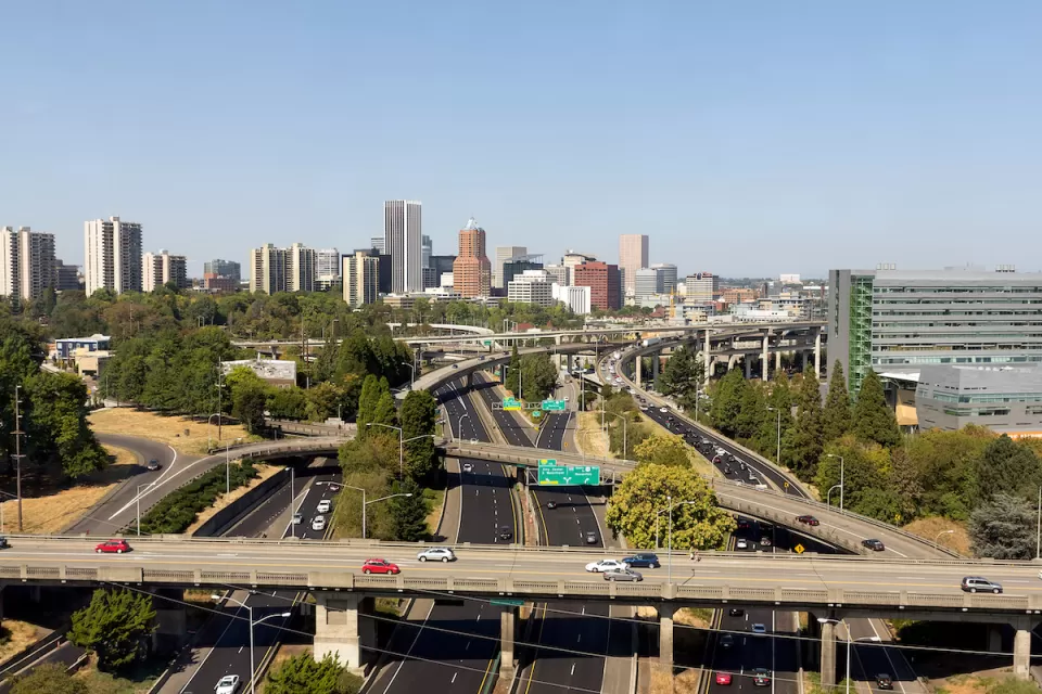 Aerial view of highway overpasses with Portland, Oregon skyline in background.